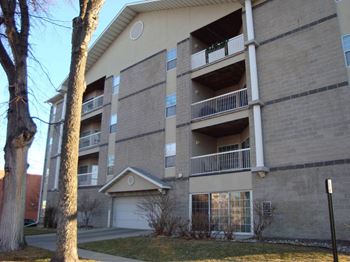 An apartment building with a garage and a tree in the foreground